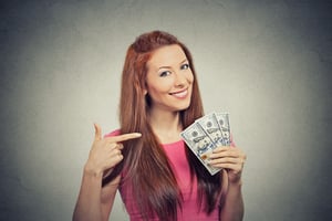 Closeup portrait super happy excited successful young business woman holding money dollar bills in hand isolated grey wall background. Positive emotion facial expression feeling. Financial reward