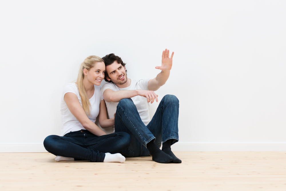 Young couple visualizing the decor of their new home sitting on the bare wooden floor pointing out and discussing placement of furniture